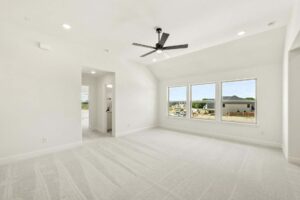 Bright, empty room with light carpet, large windows showing a neighborhood view in Painted Tree McKinney, ceiling fan, recessed lighting; doorway leads to another area.