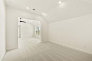 A spacious empty room with light-colored carpet, white walls, recessed lighting, and an open doorway leading to another area with a ceiling fan and windows—perfect for those seeking Painted Tree McKinney homes for sale.