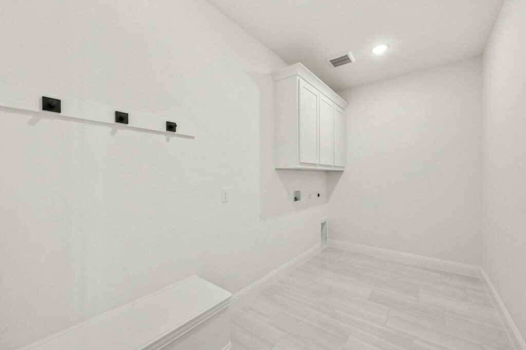 A bright, empty laundry room with white walls, upper cabinets, tile flooring, and washer/dryer hookups—just one of the inviting spaces in homes for sale in McKinney Texas at Painted Tree.