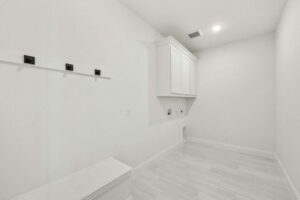 A bright, empty laundry room with white walls, upper cabinets, tile flooring, and washer/dryer hookups—just one of the inviting spaces in homes for sale in McKinney Texas at Painted Tree.