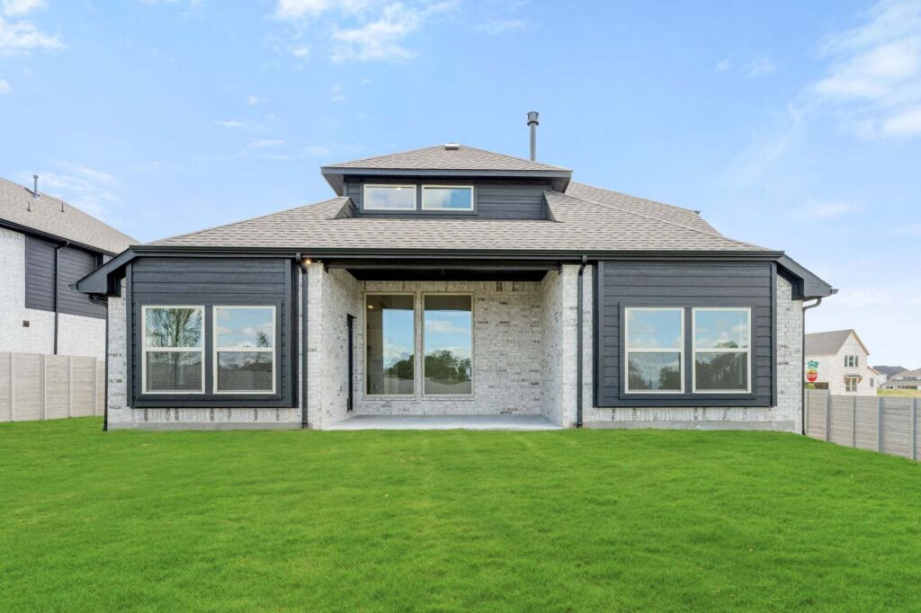 A modern two-story house with large windows, a covered patio, and a green lawn under a blue sky—perfect for those seeking homes for sale in McKinney, Texas within the desirable Painted Tree community.