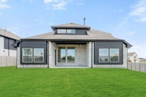 A modern two-story house with large windows, a covered patio, and a green lawn under a blue sky—perfect for those seeking homes for sale in McKinney, Texas within the desirable Painted Tree community.