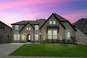 A two-story modern brick house with large windows, a manicured lawn, and a driveway, photographed at sunset under a pink and purple sky—one of the stunning painted tree homes for sale in McKinney, Texas.