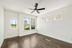 Empty room with wood flooring, white walls, ceiling fan, and large windows plus three high transom windows letting in natural light—perfect for those seeking homes for sale in McKinney Texas or exploring the Painted Tree McKinney community.