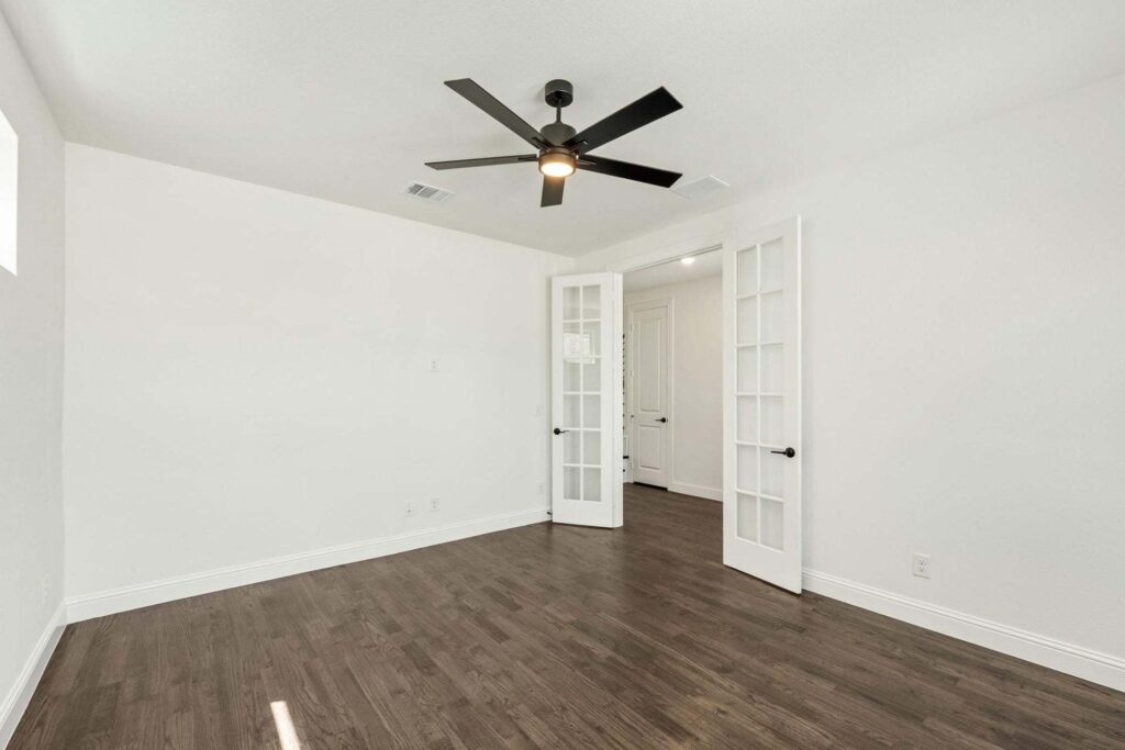 Empty room with white walls, dark wood flooring, a black ceiling fan, and double glass French doors—perfect for those searching homes for sale in McKinney Texas or looking at Painted Tree TX properties.