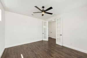 Empty room with white walls, dark wood flooring, a black ceiling fan, and double glass French doors—perfect for those searching homes for sale in McKinney Texas or looking at Painted Tree TX properties.