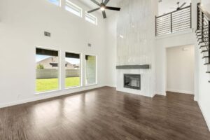 Spacious living room with high ceiling, large windows, dark wood floors, modern fireplace, ceiling fan, and a metal-railed staircase—discover homes for sale in McKinney Texas like this in the beautiful Painted Tree community.