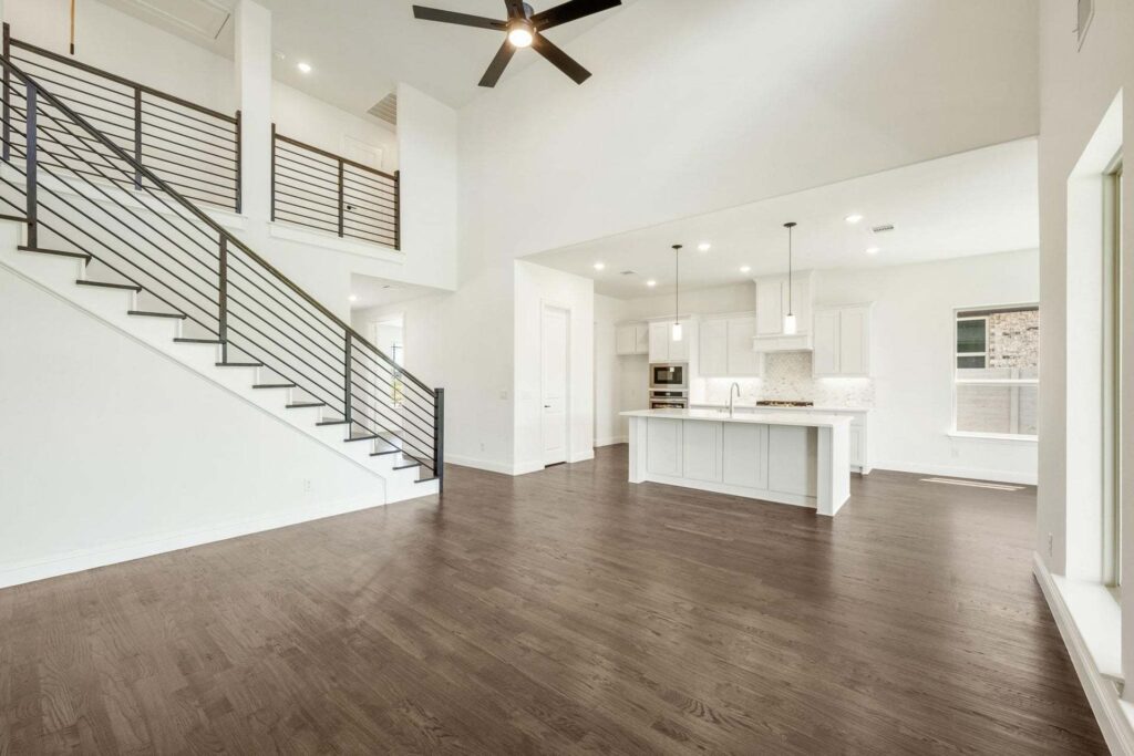 Modern open-concept living space with dark wood floors, white walls, kitchen island, pendant lighting, and a staircase with black metal railing—perfect for those seeking painted tree homes for sale in McKinney, Texas.