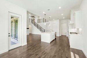 Modern open-concept kitchen and living area with white cabinets, island, wood flooring, staircase with metal railing, and glass door leading outside—perfect for those seeking homes for sale in McKinney Texas.