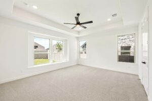 Bright empty room in Painted Tree McKinney with beige carpet, large windows, white walls, a black ceiling fan, and a tray ceiling.