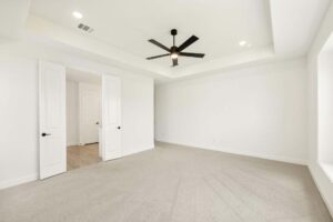 Empty, carpeted room with white walls, double doors, large window, and a ceiling fan with a light fixture—perfect for those seeking homes for sale in McKinney, Texas or exploring Painted Tree McKinney living.