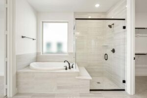 Modern bathroom with a built-in bathtub, a glass-enclosed shower, large frosted window, and neutral tile walls and floors—an inviting retreat found in the stylish homes for sale in McKinney, Texas.