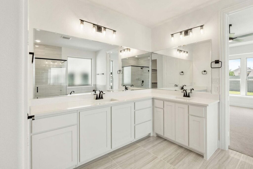 Modern bathroom with white cabinets, double sinks, large mirrors, and black fixtures. A glass shower and frosted window are visible—ideal for those seeking Painted Tree homes for sale or exploring homes for sale in McKinney Texas.