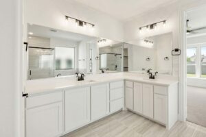 Modern bathroom with white cabinets, double sinks, large mirrors, and black fixtures. A glass shower and frosted window are visible—ideal for those seeking Painted Tree homes for sale or exploring homes for sale in McKinney Texas.