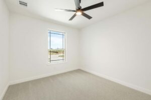 Empty room with white walls, beige carpet, large window with outdoor views, and a black ceiling fan with light—discover comfortable living in Painted Tree McKinney. Explore more Painted Tree homes for sale today!.