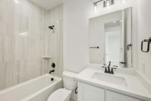 Modern bathroom in Painted Tree McKinney featuring a bathtub and shower, white countertop and cabinets, large mirror, toilet, and sleek black fixtures—perfect for those seeking stylish homes for sale in McKinney, Texas.