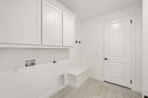 A laundry room with white cabinets, hookups for a washer and dryer, a utility bench, and a closed white door—perfectly designed for convenience in the beautiful Painted Tree McKinney community.