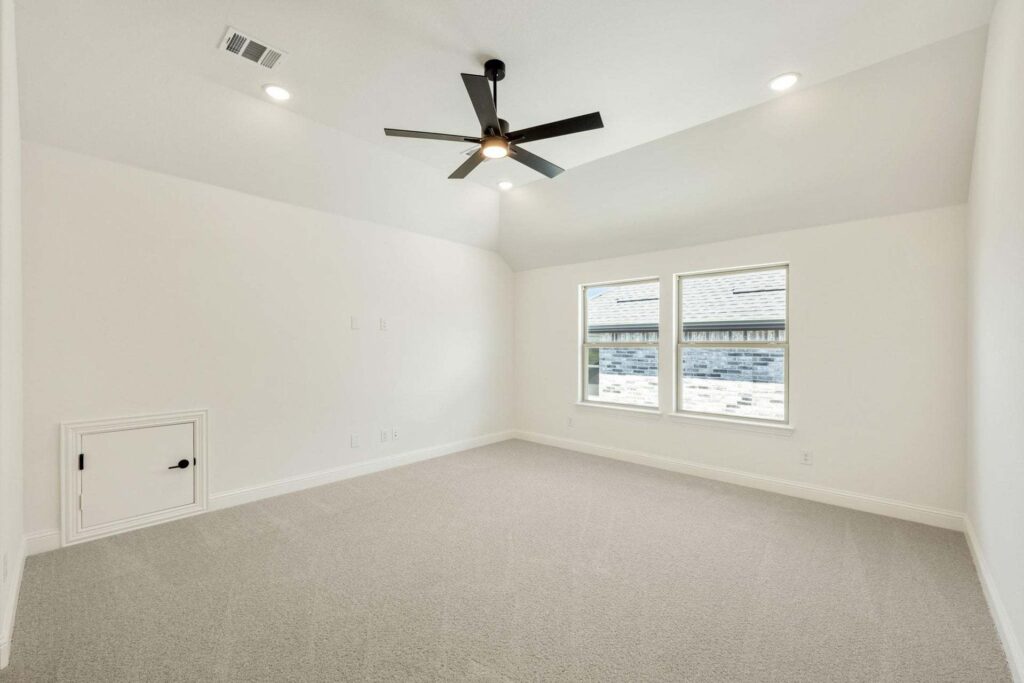 Empty, carpeted room with white walls, black ceiling fan, recessed lighting, two windows, and a small door—perfect for relaxing in one of the beautiful Painted Tree homes for sale in McKinney, Texas.