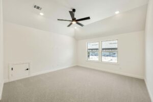 Empty, carpeted room with white walls, black ceiling fan, recessed lighting, two windows, and a small door—perfect for relaxing in one of the beautiful Painted Tree homes for sale in McKinney, Texas.