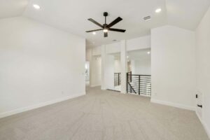 Spacious, empty room with light beige carpet, white walls, black ceiling fan, recessed lighting, and metal railing overlooking a lower level—perfect for those seeking Painted Tree McKinney homes for sale.