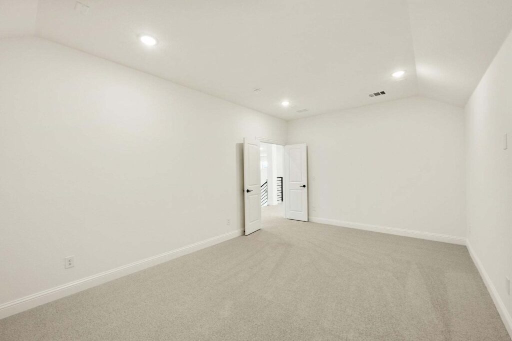 Empty, carpeted room with white walls, recessed ceiling lights, and double doors opening to a hallway—an inviting space found in many Painted Tree homes for sale in McKinney, Texas.