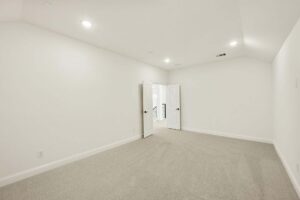 Empty, carpeted room with white walls, recessed ceiling lights, and double doors opening to a hallway—an inviting space found in many Painted Tree homes for sale in McKinney, Texas.