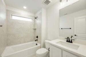 Modern bathroom in Painted Tree TX with a white bathtub and shower, beige tiled walls, a toilet, white vanity with sink, large mirror, and sleek black fixtures—discover stylish details in homes for sale in McKinney Texas.