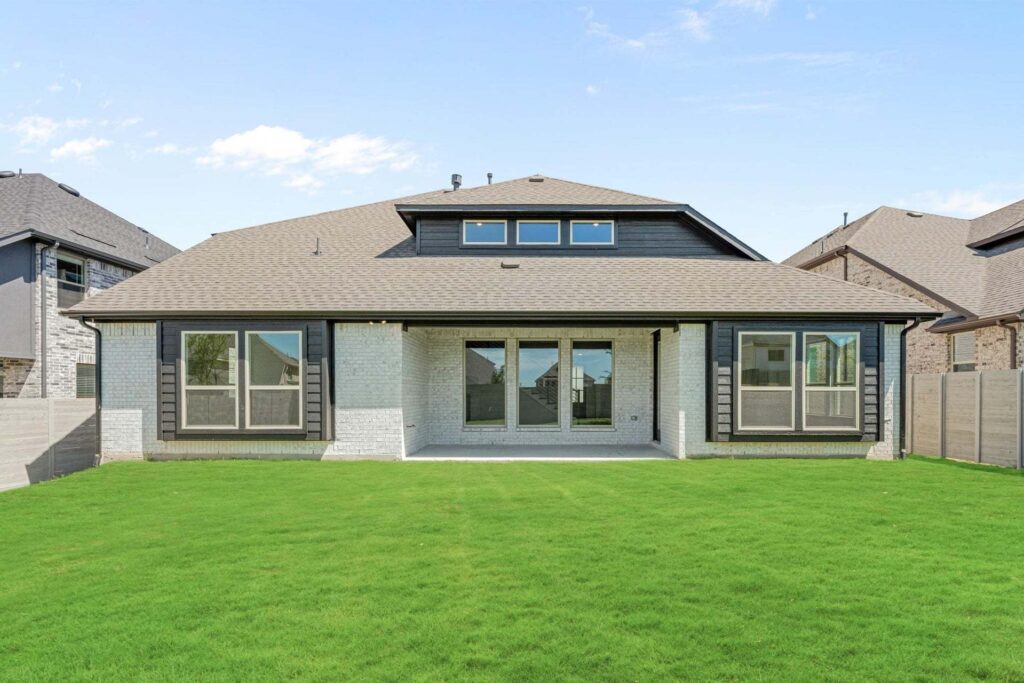 A modern single-story house with large windows and a covered patio, viewed from a backyard with well-maintained green grass in Painted Tree McKinney, offers stylish living among sought-after homes for sale in McKinney, Texas.