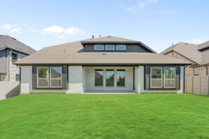 A modern single-story house with large windows and a covered patio, viewed from a backyard with well-maintained green grass in Painted Tree McKinney, offers stylish living among sought-after homes for sale in McKinney, Texas.