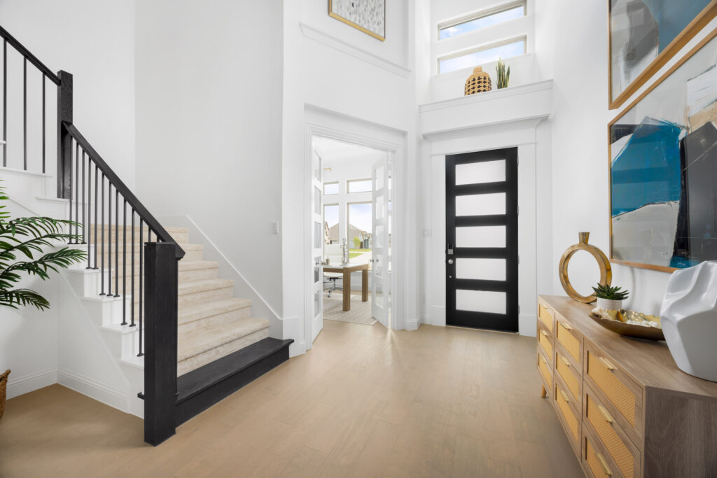 Bright, modern entryway in a Coventry Homes property in McKinney, TX, featuring a black and white door, staircase with beige carpet, light wood floor, and contemporary decor leading into a sunlit room.