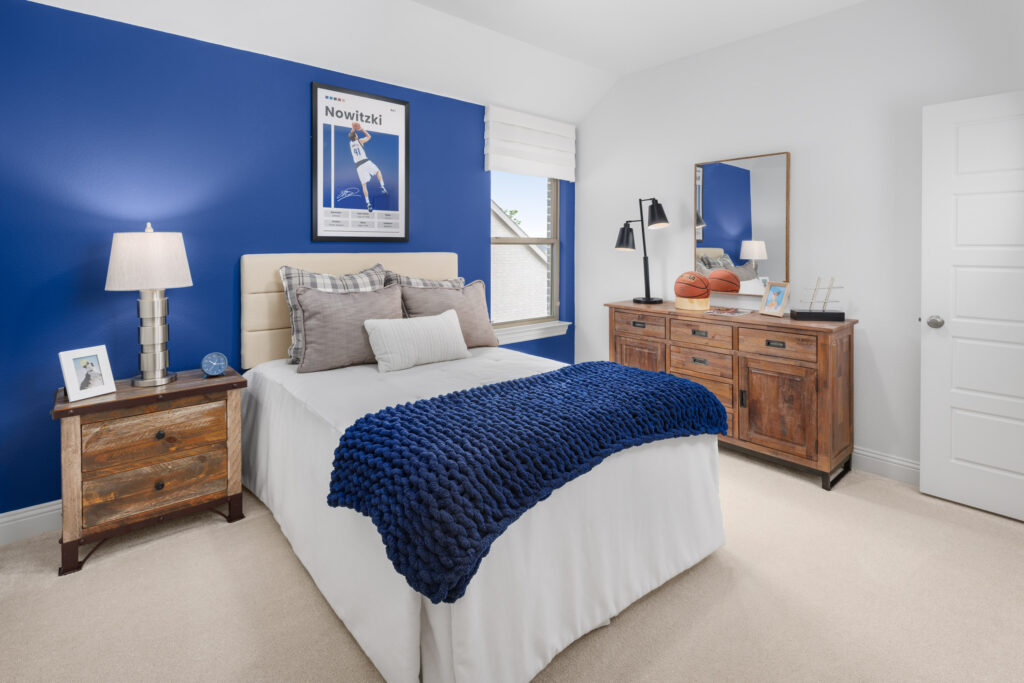 A bedroom in McKinney with a white bed, blue accent wall, wooden furniture, sports decor, and a Nowitzki basketball poster above the bed showcases the modern style found in Coventry Homes at Painted Tree.