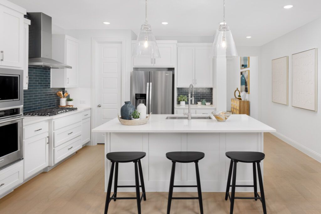 Modern kitchen with white cabinets, stainless steel appliances, a central island with sink, three black stools, pendant lights, and minimalist decor in the heart of Painted Tree, McKinney, TX.
