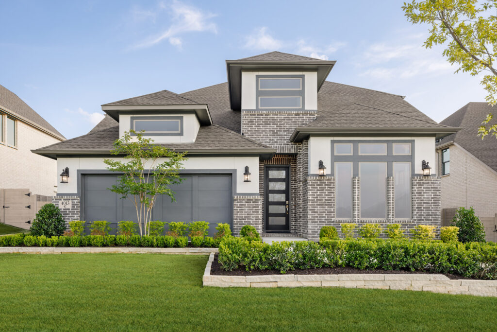 Modern two-story Coventry Homes new home in McKinney with gray brick exterior, large windows, double garage, manicured lawn, and landscaped front yard under a clear blue sky.