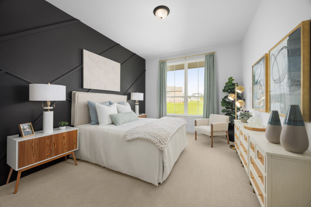 Modern bedroom with a black accent wall, neatly made bed, two nightstands, dresser, and armchair. Large window fills the space with natural light in this Painted Tree home in McKinney, TX.