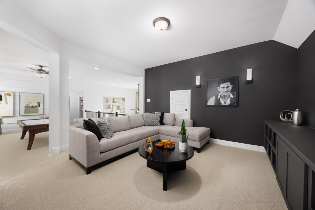 A modern living room in a new home by Coventry Homes at Painted Tree, featuring a gray sectional sofa, black accent wall, monochrome portrait, round black coffee table, and built-in cabinetry next to the game area.