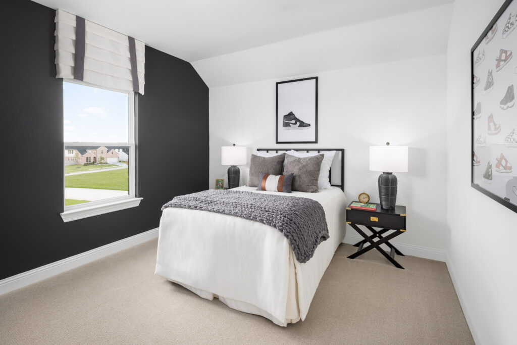 A modern bedroom in Painted Tree, McKinney, features a single bed with gray and white bedding, two black nightstands with lamps, a window, and framed sneaker artwork on the walls—perfect for your new home.