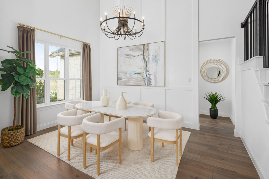 Modern dining room in McKinney, TX featuring a round white table, six beige chairs, three vases, a chandelier, abstract wall art, large window overlooking Painted Tree, potted plant, and stylish wood flooring.