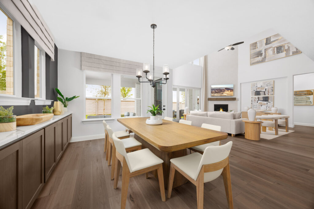 Modern open-concept dining and living room in a Coventry Homes new home at Painted Tree, featuring light wood floors, large windows, neutral decor, and a wooden dining table surrounded by white chairs.