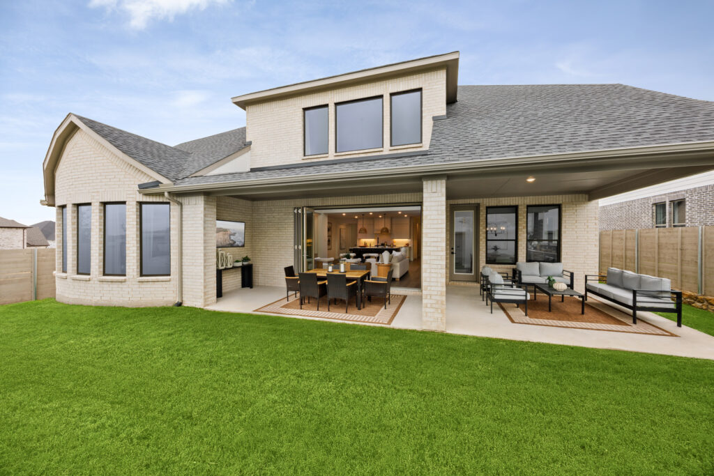 Modern Coventry Homes new home with a large covered patio, outdoor dining and seating areas, and wide glass doors opening to a grassy backyard in TX.