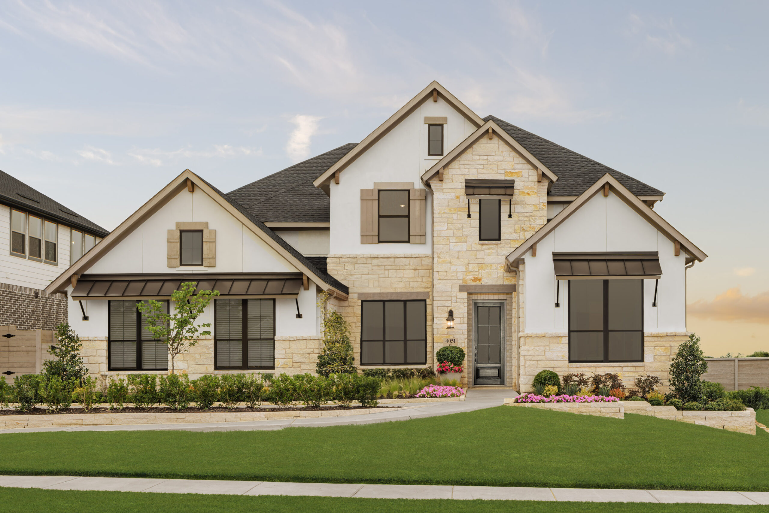 Two-story suburban house in McKinney's Painted Tree community with stone and white siding exterior, black trim, front lawn, small shrubs, and flower beds—a true TX gem.