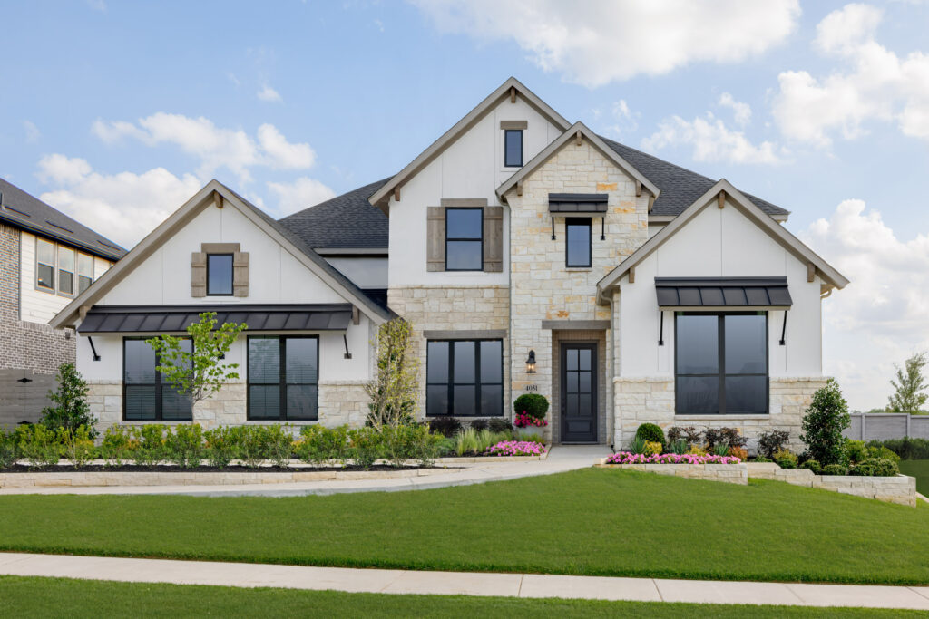 Two-story modern Coventry Homes house with stone and white siding exterior, black window frames, manicured lawn, shrubs, and a clear sky in the Painted Tree community.