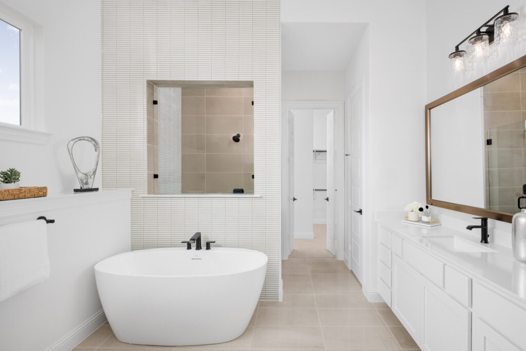 Modern bathroom in a new home at Painted Tree, TX, featuring a white freestanding tub, glass shower, double sink vanity with mirror, and minimal decor in a neutral color palette.