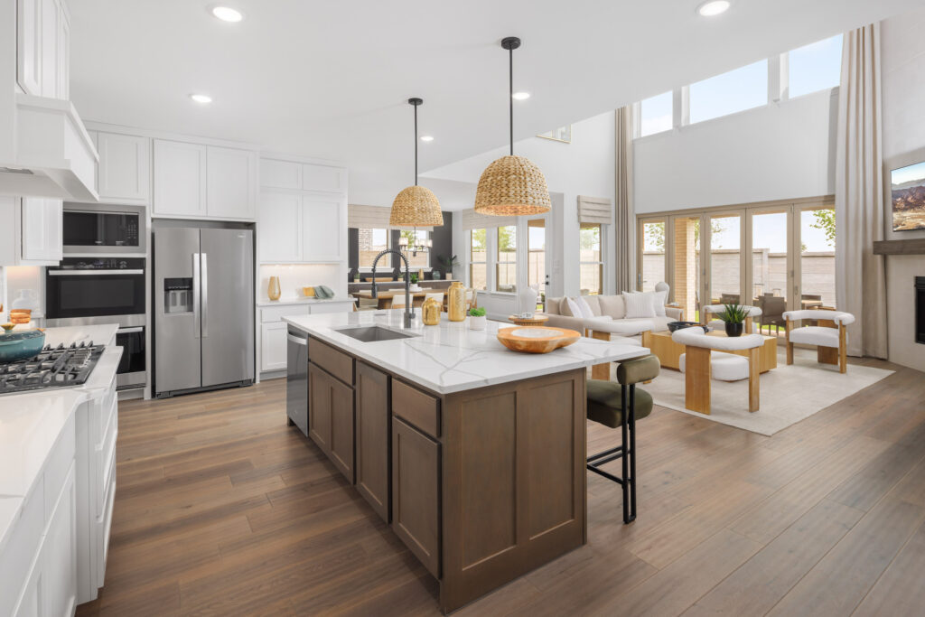 Modern kitchen by Coventry Homes with white cabinets, stainless steel appliances, a large island with wooden base, pendant lights, and an open layout leading to a bright living area in McKinney’s Painted Tree community.