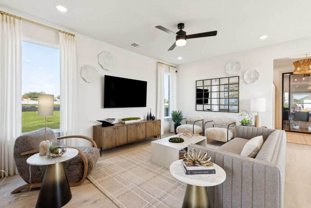 Modern living room in Painted Tree, McKinney, with neutral colors, a large wall-mounted TV, minimalist furniture, decorative wall art, and natural light from tall windows—perfect for stylish new homes.