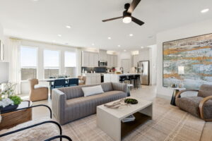 Modern open-concept living room and kitchen in Normandy Homes at Painted Tree, McKinney, featuring neutral colors, large windows, contemporary furniture, and a ceiling fan.