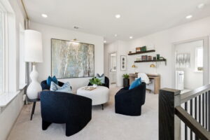 Modern living room in McKinney with four black chairs, a round ottoman, large abstract wall art, desk with shelves, and neutral decor. Natural light fills this stylish space by Normandy Homes.