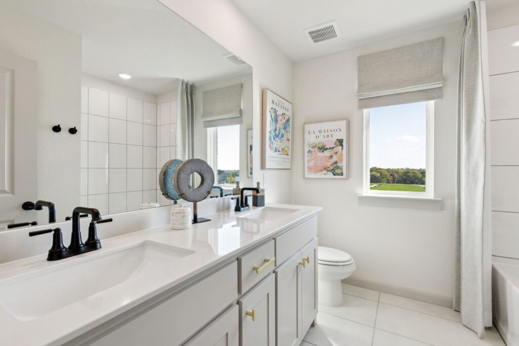 Modern bathroom with double sink vanity, black fixtures, decorative art on the wall, and a window with a view outside—experience elevated style in this Normandy Homes Painted Tree residence in McKinney.