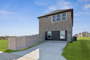 Discover this two-story brick house in Painted Tree, McKinney. Enjoy a black garage door, concrete driveway, and fenced side yard—all on a grassy lot beneath a clear sky. Explore the finest new homes today!.