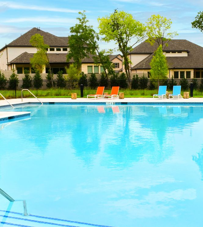 Large outdoor swimming pool with calm water, four colorful lounge chairs, metal handrails, and residential houses in the background under a blue sky—an inviting Pool setting near the Lakeside Trailhead in McKinney, TX.